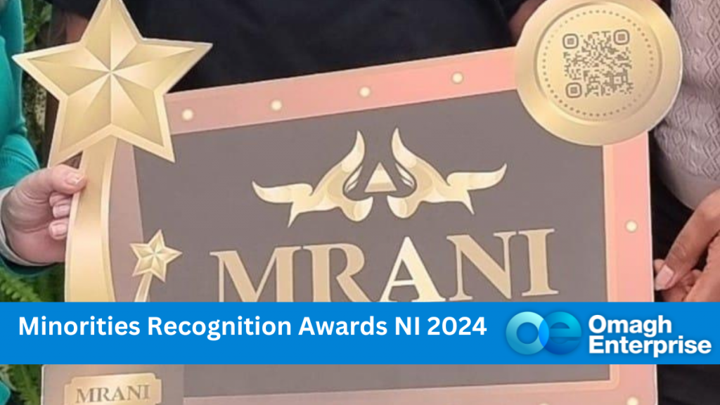 Two PoC hands holding a MRANI board, to launch the award. Blue Banner long the bottom. White text "Minorities Recognition Awards NI 2024" . Omagh Enterprise logo within the banner