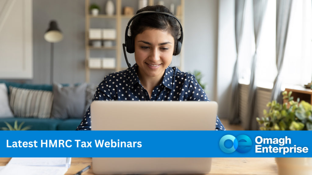 A woman in a black top, with white dots. She is wearing headphones, with a mic and working on her laptop. Blue banner along the bottom. White text "Latest HMRC Tax Webinars" Omagh Enterprise logo within the blue banner.