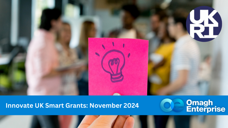 A person holds a pink sticky note with a light bulb drawing. In the background, a diverse group is blurred. The image features logos for UKRI and Omagh Enterprise, and text reads Innovate UK Smart Grants: November 2024.