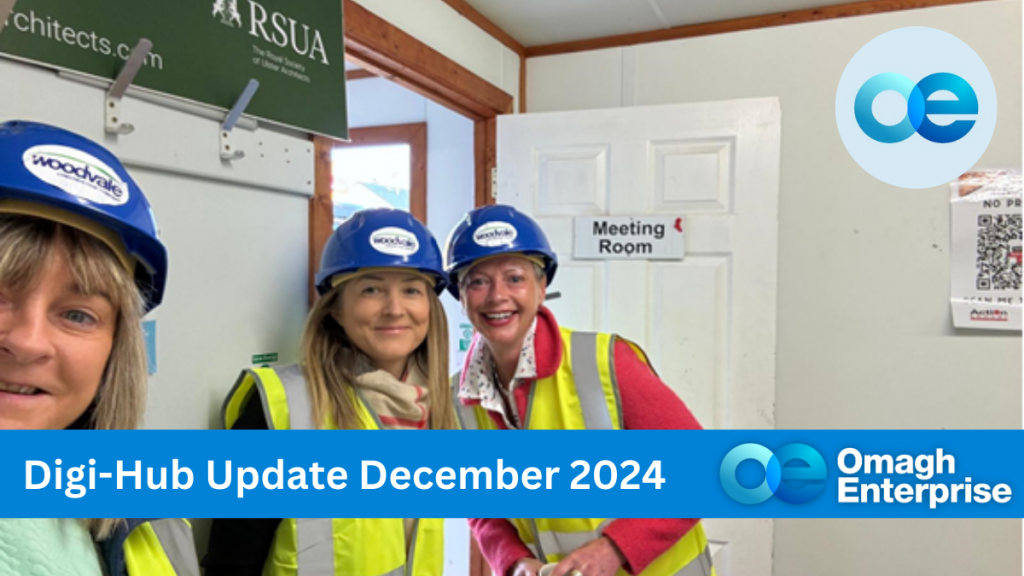 Mary Mac Rory, Julie McCausland and Sharon Tracey-Collins are wearing blue hard hats and yellow safety vests stand smiling in front of a door labeled Meeting Room. The image has text saying Digi-Hub Update December 2024 and Omagh Enterprise.