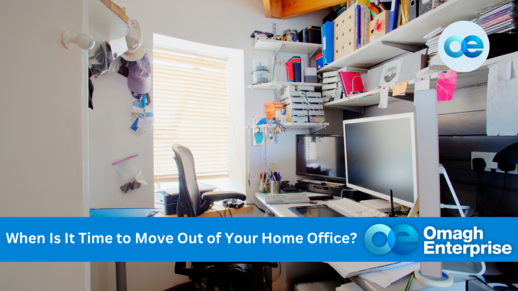 A cluttered home office with a desk, multiple monitors, shelves filled with books and boxes, and a window with blinds. Text "When Is It Time to Move Out of Your Home Office?"