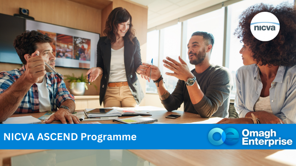 A group of four people engaged in a meeting around a table. A smiling woman stands while others sit, discussing. Papers and electronic devices are on the table. Logos for NICVA and Omagh Enterprise are overlaid with text NICVA ASCEND Programme.