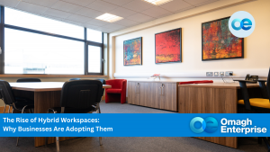 Office space with large windows, wooden desks, colorful chairs, and framed abstract art. Text overlay: "The Rise of Hybrid Workspaces: Why Businesses Are Adopting Them. Omagh Enterprise.