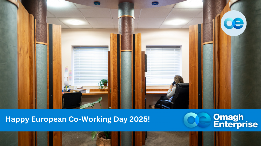 Person sitting in a private co-working booth with wooden panels, talking on a phone. Banner at the bottom reads "Happy European Co-Working Day 2025! Omagh Enterprise." Logo in the top corner.