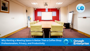 An Omagh Enterprise meeting room with a large table and yellow chairs. The walls are white and a red accent wall is at the far end. There's a screen and presentation equipment.