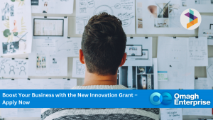 A person looks at a bulletin board filled with papers and diagrams. Banner text: "Boost Your Business with the New Innovation Grant – Apply Now. Omagh Enterprise.