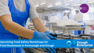 Two workers in blue aprons handle food in a clean facility. Text overlay promotes food safety workshops for businesses in Fermanagh and Omagh.