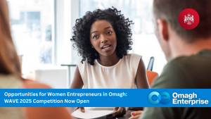 A woman speaks to two people at a table. Banner text reads: "Opportunities for Women Entrepreneurs in Omagh: WAVE 2025 Competition Now Open. Omagh Enterprise.