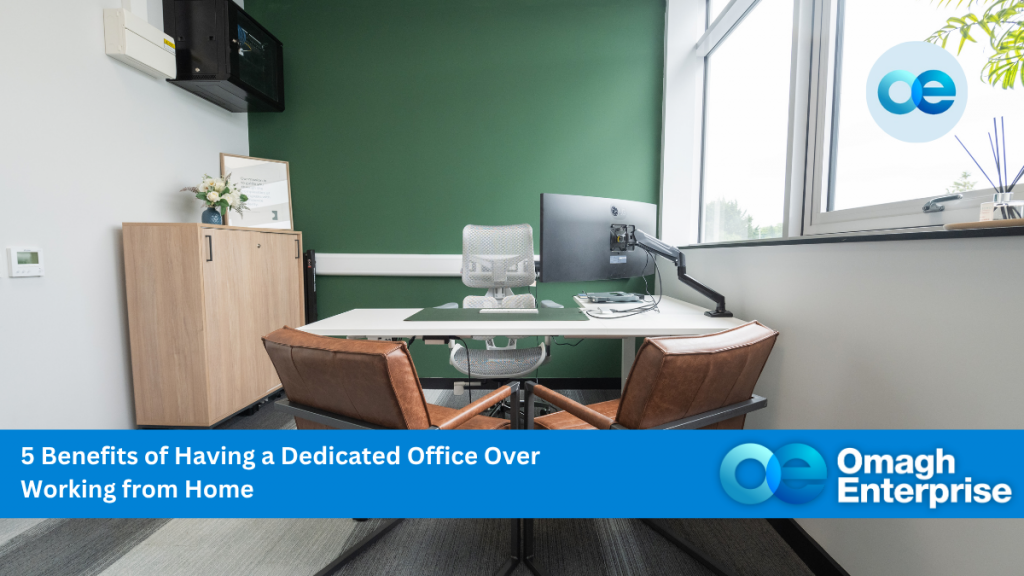 Modern office at Omagh Digi-Hub with a desk, two chairs, computer monitor, and green accent wall. Text overlay reads: "5 Benefits of Having a Dedicated Office Over Working from Home. Omagh Enterprise.