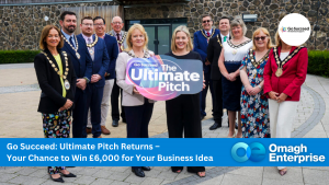 A group of people, including Councillor Shirley Hawkes, Vice Chair of Fermanagh and Omagh District Council, wearing ceremonial chains, stand outside holding a sign that reads “The Ultimate Pitch.” Text overlay promotes a chance to win £6,000 for a business idea from Go Succeed and Omagh Enterprise.