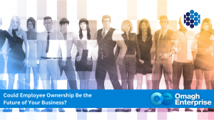 A diverse group of people stands together behind a blue banner that reads, "Could Employee Ownership Be the Future of Your Business? Omagh Enterprise.
