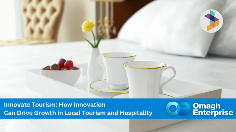 A white tray with two teacups, a teapot, and a bowl of strawberries on a neatly made bed; promotional banner for Omagh Enterprise’s tourism innovation event.