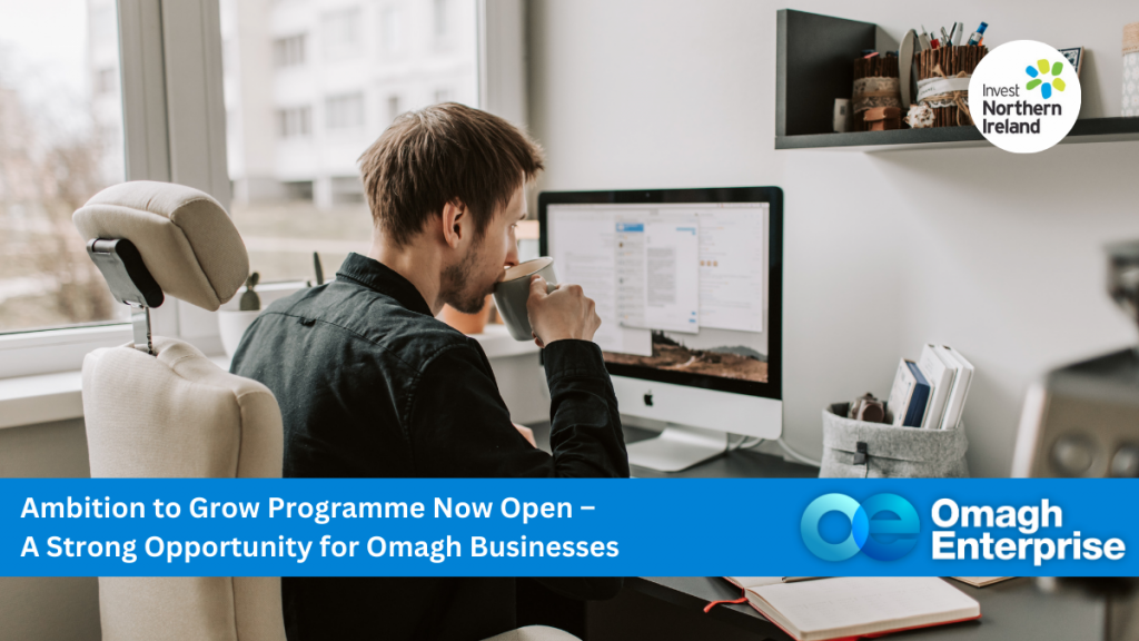 A man sits at a desk in a home office, drinking from a mug while working on a computer. Banner text promotes the "Ambition to Grow Programme" by Omagh Enterprise and Invest Northern Ireland.