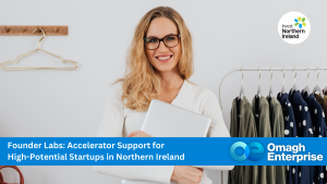 A woman holding a laptop stands in front of a clothing rack. Text overlay promotes accelerator support for startups in Northern Ireland by Omagh Enterprise and Invest Northern Ireland.