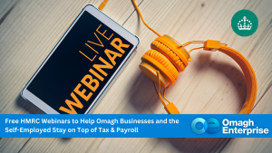 A smartphone showing "LIVE WEBINAR" next to orange headphones on a wooden surface, with a banner about HMRC webinars for Omagh businesses and the self-employed.