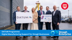 Six people in business attire stand outside holding signs for the DATUM Programme and PEACEPLUS, promoting digital manufacturing support for Omagh businesses.