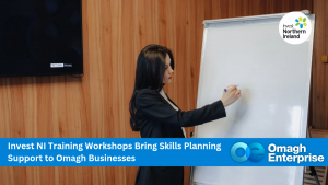 A woman writes on a flip chart during a business workshop. The banner promotes Invest NI training for Omagh businesses.