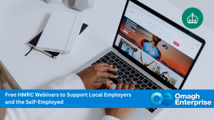 Person typing on a laptop with a website open, notebook and pen nearby. Banner reads: "Free HMRC Webinars to Support Local Employers and the Self-Employed. Omagh Enterprise.