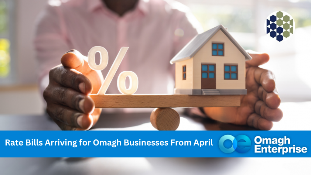 A person holds a seesaw with a percentage symbol and a small house, with text announcing rate bills for Omagh businesses from April and the Omagh Enterprise logo.