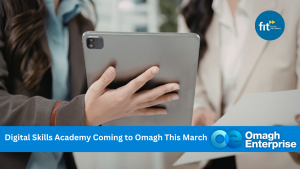 Two people in business attire hold a tablet and documents. A banner reads, "Digital Skills Academy Coming to Omagh This March" with FIT and Omagh Enterprise logos.