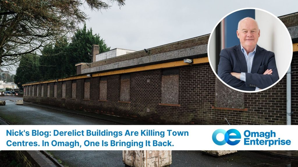The boarded-up derelict brick old Health Centre building with a cloudy sky; inset shows Nick in a suit standing with arms crossed, accompanied by the Omagh Enterprise logo and blog headline text.