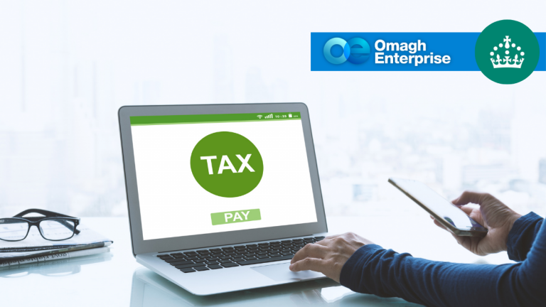 A person uses a laptop displaying a green TAX button and PAY option, while holding a smartphone. The Omagh Enterprise logo and a crown symbol appear in the top right corner.