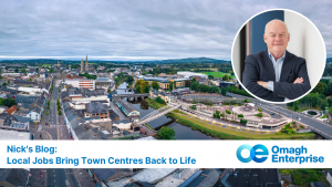 Aerial view of Omagh town centre with buildings, a river, and green hills; inset photo of Nick in a suit; text: "Nick's Blog: Local Jobs Bring Town Centres Back to Life. Omagh Enterprise.