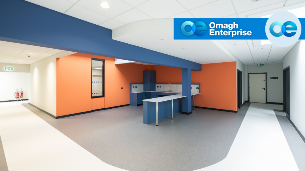 A modern, empty interior space with orange and white walls, blue structural elements, grey flooring, and a central blue counter under bright lighting.