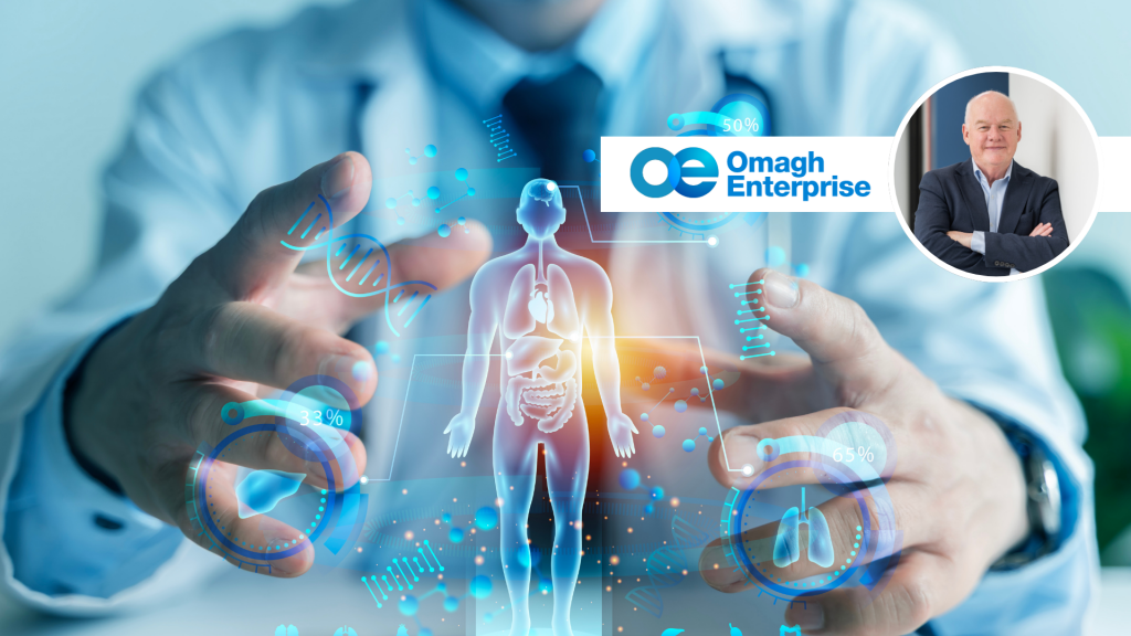 A doctor in a white coat uses a digital interface displaying a human body and medical icons. The Omagh Enterprise logo and a small photo of a man in a suit appear in the top right corner.