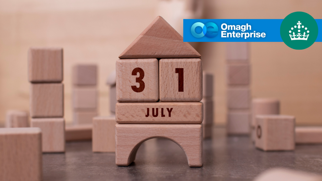 Wooden blocks arranged to form a house display the date 31 July. In the top right corner, there is a blue banner with the Omagh Enterprise logo and a crown icon on a green circle.