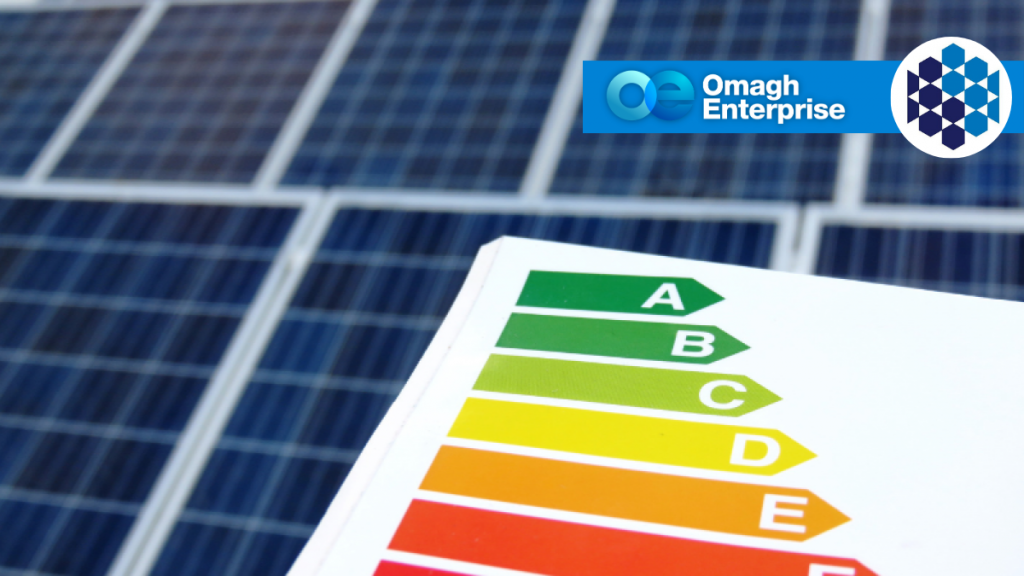 A close-up of a colorful energy efficiency rating chart in front of solar panels, with the Omagh Enterprise logo in the background.
