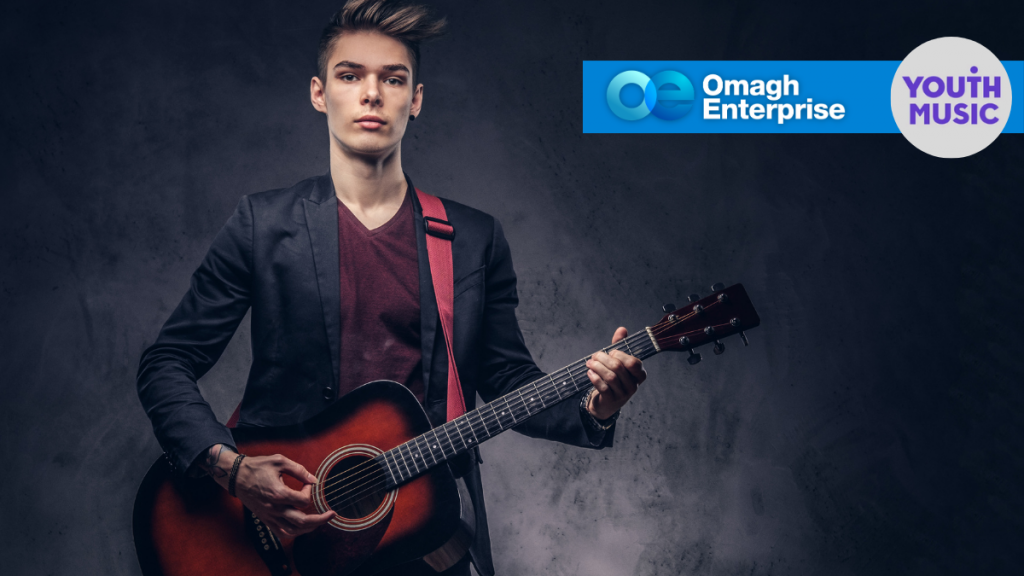 Young person playing an acoustic guitar, wearing a dark blazer and red shirt. Omagh Enterprise and Youth Music logos appear in the upper right corner.