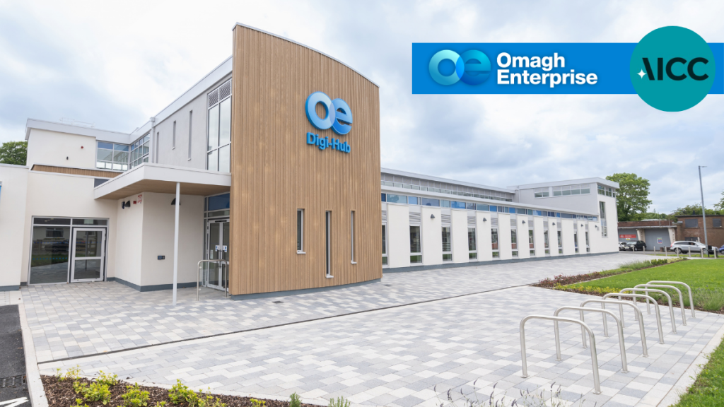 Modern office building with “Digi-Hub” and “Omagh Enterprise” signage, bike racks, paved walkway, and landscaped greenery under a cloudy sky.