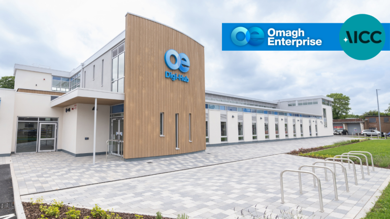 Modern office building with “Digi-Hub” and “Omagh Enterprise” signage, bike racks, paved walkway, and landscaped greenery under a cloudy sky.