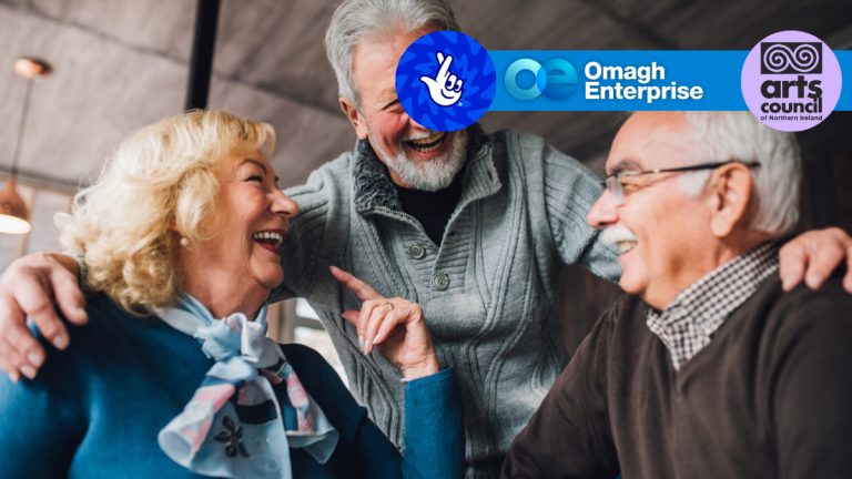 Three older adults sit together indoors, smiling and laughing. Logos for Omagh Enterprise, the Arts Council of Northern Ireland, and the National Lottery are displayed at the top of the image.