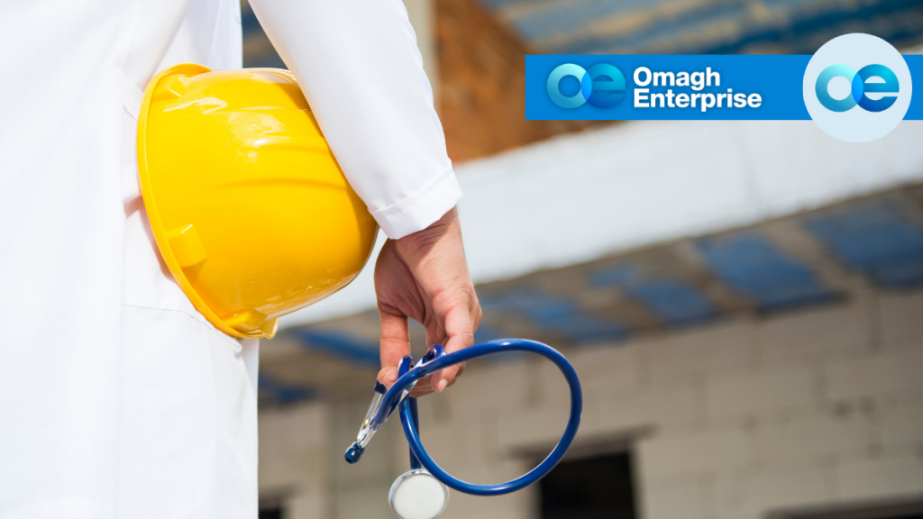 Person in a white coat holding a yellow hard hat and a stethoscope, with the Omagh Enterprise logo in the top right corner.