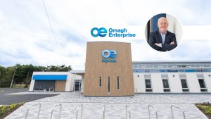 Modern Digi-Hub building with “Omagh Enterprise” and “Digi-Hub” logos on the facade, with a circular inset photo of Nick in a suit in the upper right corner.