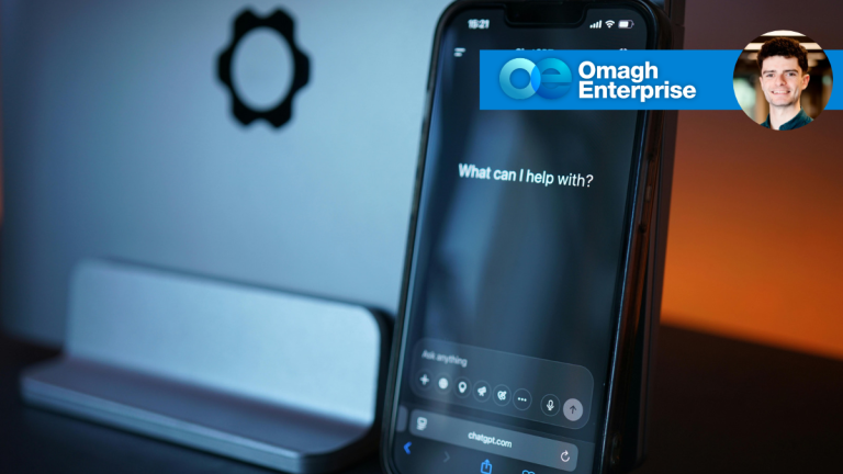 A smartphone on a stand displays the ChatGPT interface with the prompt, “What can I help with?”.