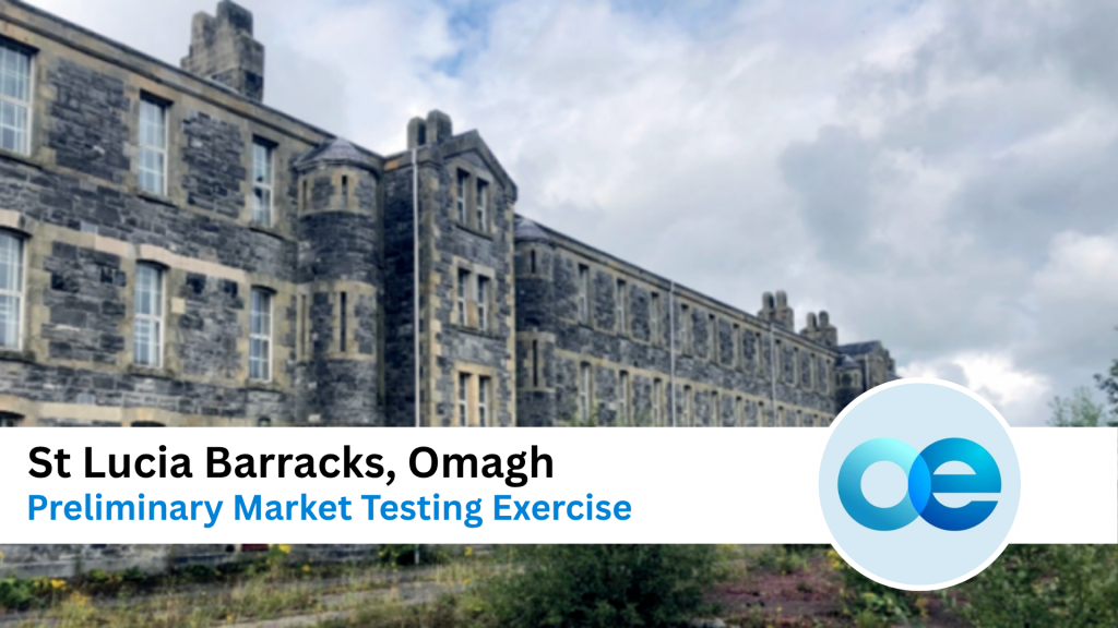 A large, old stone building labeled St Lucia Barracks, Omagh, with cloudy skies above and overgrown vegetation in the foreground.
