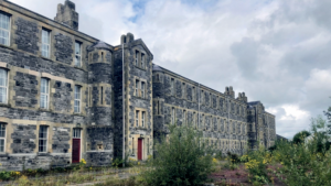 The former St Lucia Barracks buildings in Omagh, with grass and overgrowth in the foreground."