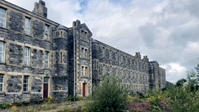 The former St Lucia Barracks buildings in Omagh, with grass and overgrowth in the foreground."